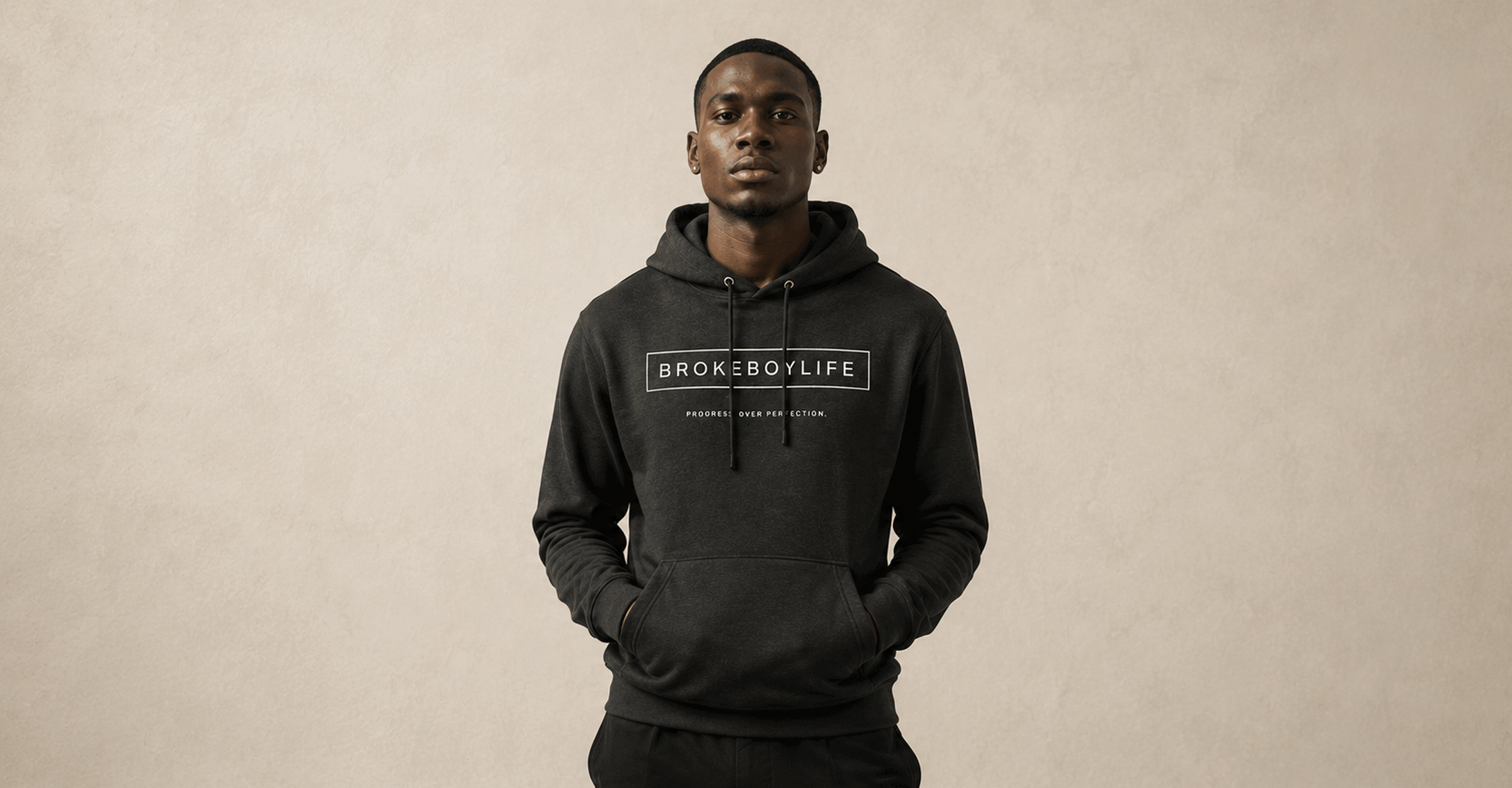 Model wearing the black BROKEBOYLIFE hoodie featuring the signature logo and "Progress Over Perfection" design.